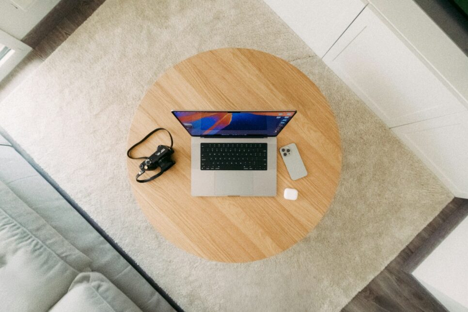 Laptop, camera, and phone on a wooden table.