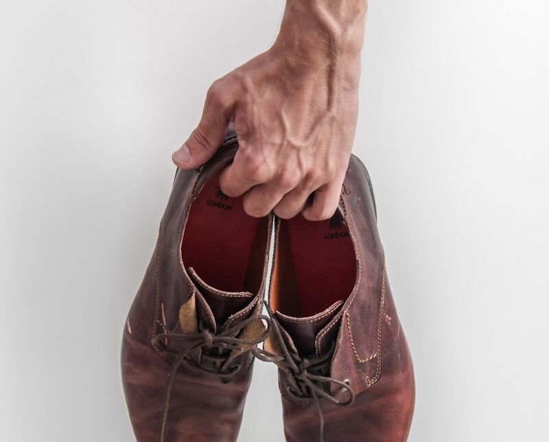 person holding pair of brown leather shoes