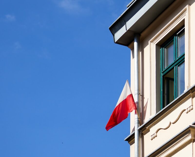 a red and white flag on a pole in front of a building