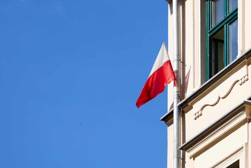 a red and white flag on a pole in front of a building