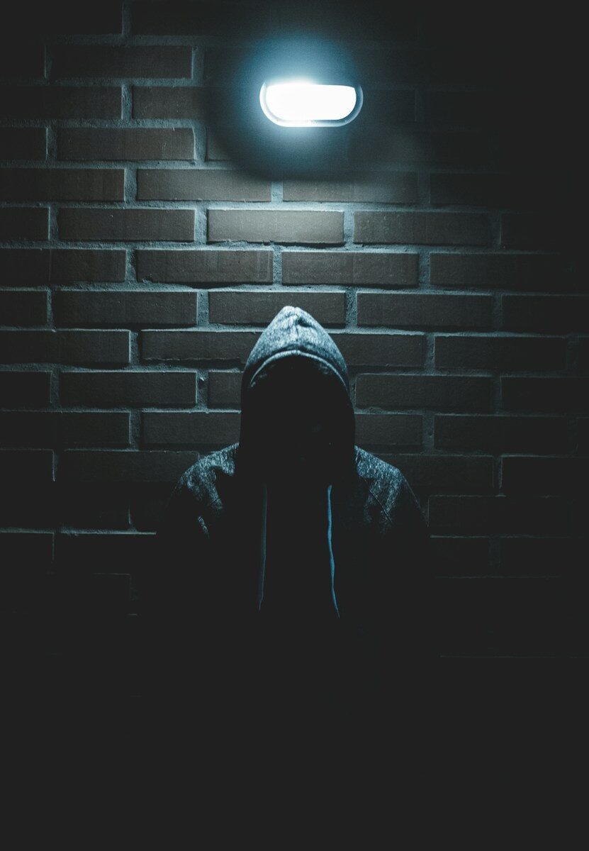 A person in a hooded sweatshirt in silhouette against a dark brick wall